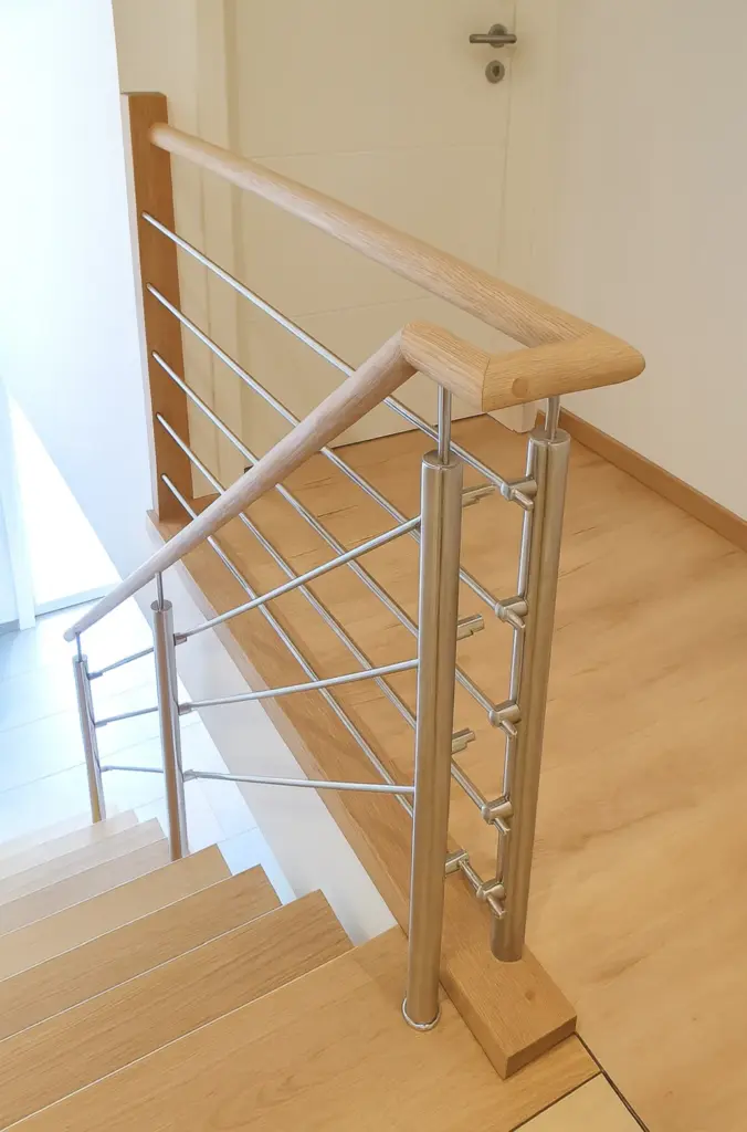 Moderne Innentreppe mit hellen Holzstufen und Handlauf, mit einem eleganten Metallgeländer mit horizontalen Stäben und vertikalen Stützen, das zu einer geschlossenen weißen Tür am oberen Ende führt.