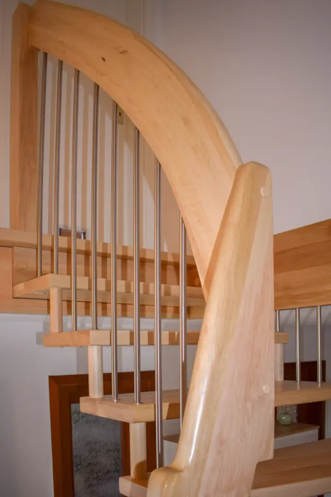 Eine moderne Holzspindeltreppe mit Metallgeländer, hellen Holzstufen und geschwungenen Handläufen, die in einem hellen Innenraum nach oben führt.