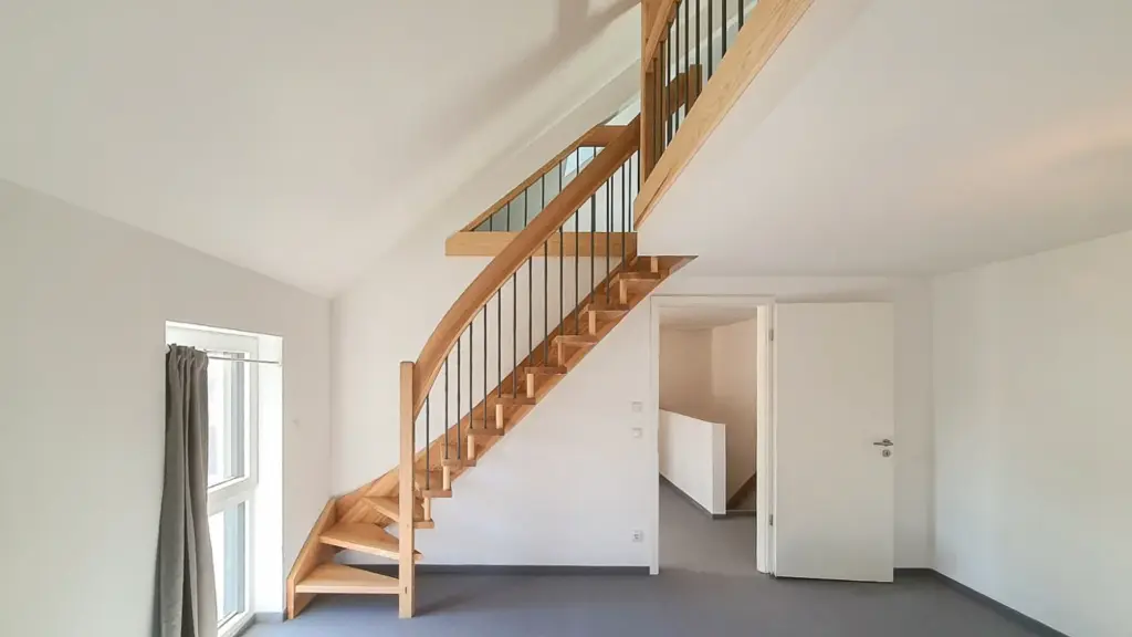 Ein moderner, minimalistischer Raum mit hellen Wänden, einem Teppichboden und einer Holztreppe mit Metallgeländer, die in ein höheres Stockwerk führt. Auf der linken Seite befindet sich ein Fenster mit einem grauen Vorhang, und eine offene Tür führt zu einem Korridor.