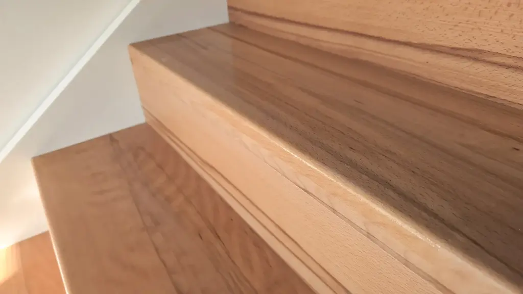 Nahaufnahme einer polierten Holztreppe mit glatter, glänzender Oberfläche und sichtbarer Holzmaserung, die in der Nähe einer weißen Wand steht.