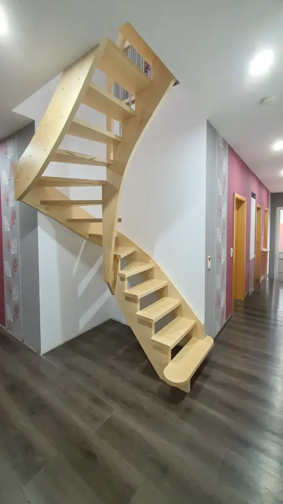 Eine moderne, minimalistische Holztreppe ohne Geländer schlängelt sich in einer Ecke eines Flurs mit grauen und rosafarbenen Tapeten und dunklem Holzfußboden nach oben. Türen säumen den Flur auf der rechten Seite.