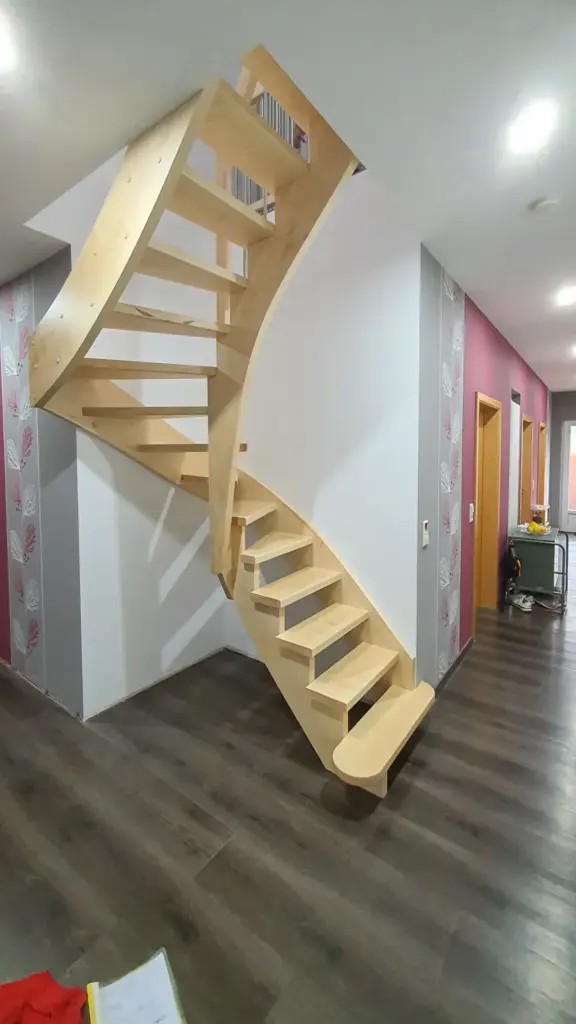Eine moderne, schwebende Holztreppe mit offenen Setzstufen wölbt sich vor einer rosa und weiß tapezierten Wand in einem modernen Wohnbereich mit dunklem Holzfußboden nach oben.