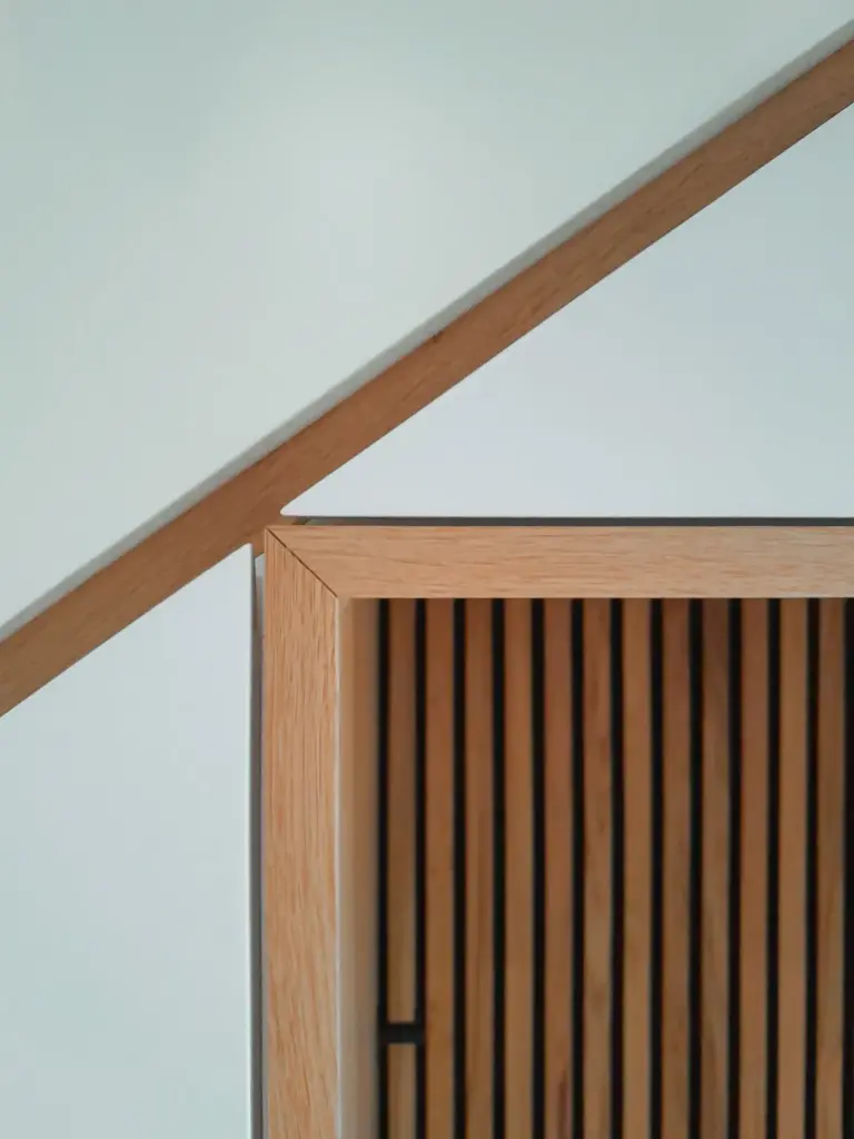 Minimalistisches architektonisches Detail mit sich kreuzenden Linien aus hellem Holz und weißen Wänden, mit einem Abschnitt aus vertikalen Holzlatten und klaren geometrischen Formen.