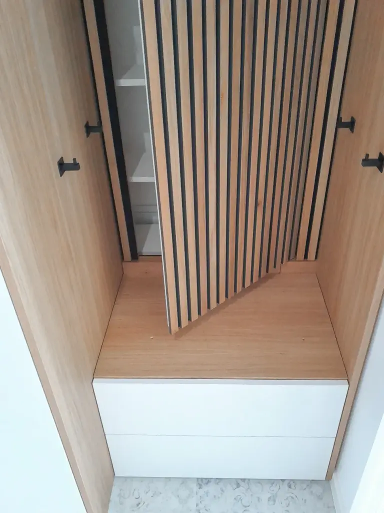 Offener hölzerner Schrank mit schwarzen vertikalen Streifen, der im Inneren weiße Einlegeböden aufweist; im unteren Teil befinden sich zwei weiße Schubladen und ein Holzpodest.