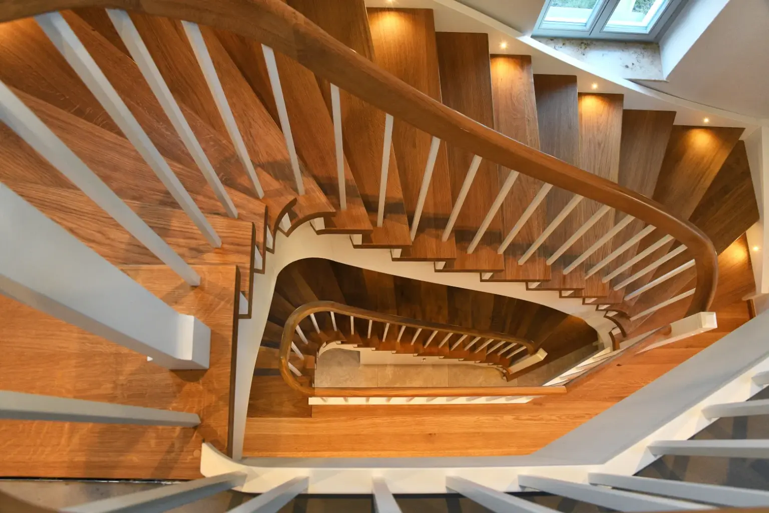 Klassische Holztreppe mit weißen Streben und Holzfarbenen Handlauf über mehrere Etagen.