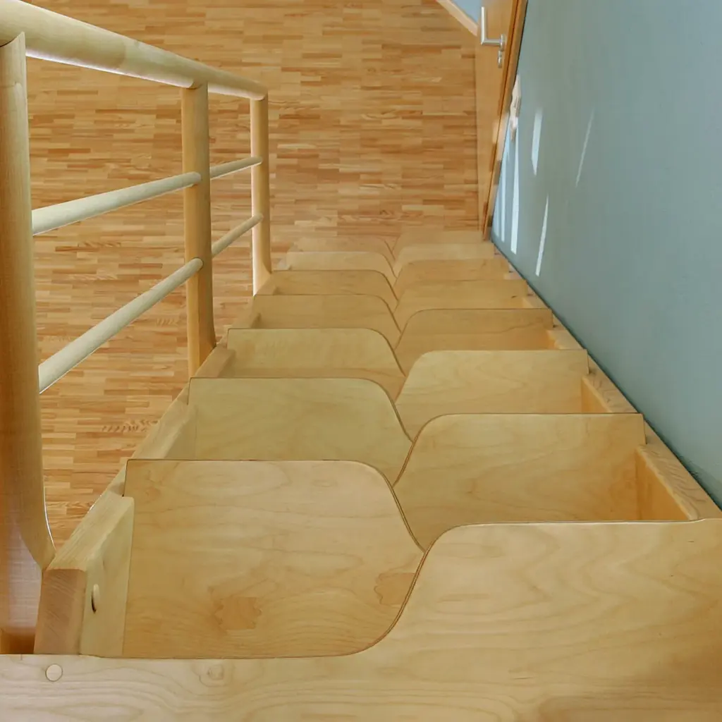 Eine Holztreppe mit abwechselnden Stufen und einem einzigartigen, platzsparenden Zickzackmuster, die zu einem polierten Holzboden und einer geschlossenen Tür auf der rechten Seite führt.