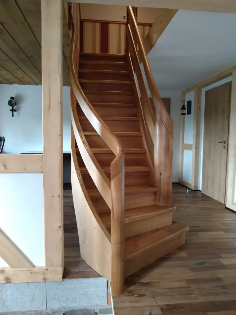 Eine Holztreppe mit geschwungenem Geländer führt zu einer oberen Etage in einem modernen Interieur mit Holzböden, -türen und -verkleidungen. Die Treppe hat eine natürliche Oberfläche und glatte, fließende Linien.