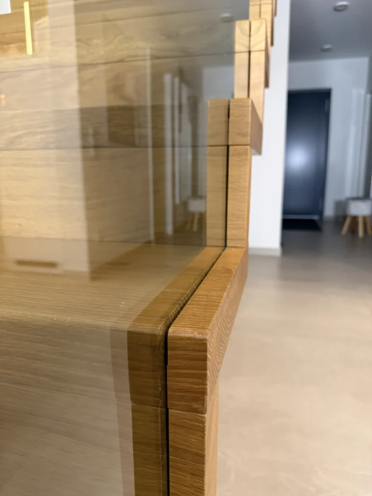 Nahaufnahme einer modernen Treppe mit Holzstufen und klaren Glaspaneelen, die ein nahtloses, minimalistisches Design in einem gut beleuchteten, zeitgenössischen Innenraum zeigt.