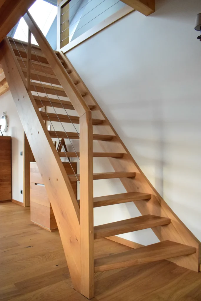 Eine moderne Holztreppe mit offenen Setzstufen und Metallgeländer, eingebettet in einen hellen Raum mit Holzfußboden und einem minimalistischen Design.