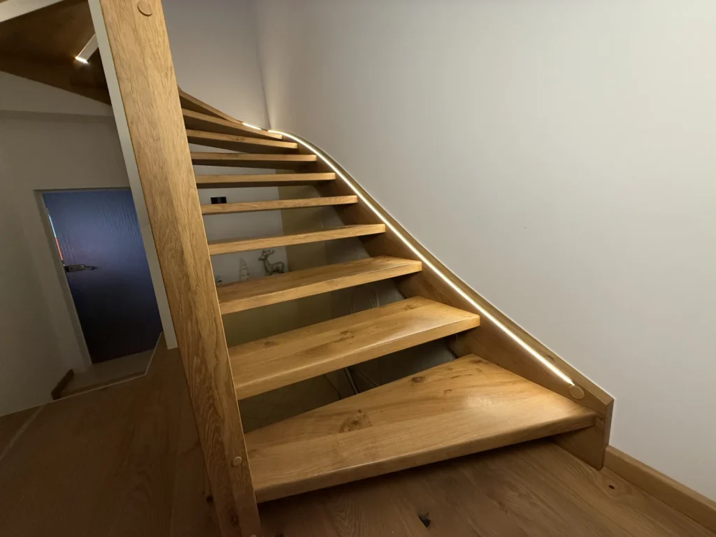 Eine moderne Holztreppe mit offenen Setzstufen und einem geschwungenen Handlauf mit eingebauten LED-Lichtbändern an der Seite, die in einem gut beleuchteten Innenraum nach oben führt.