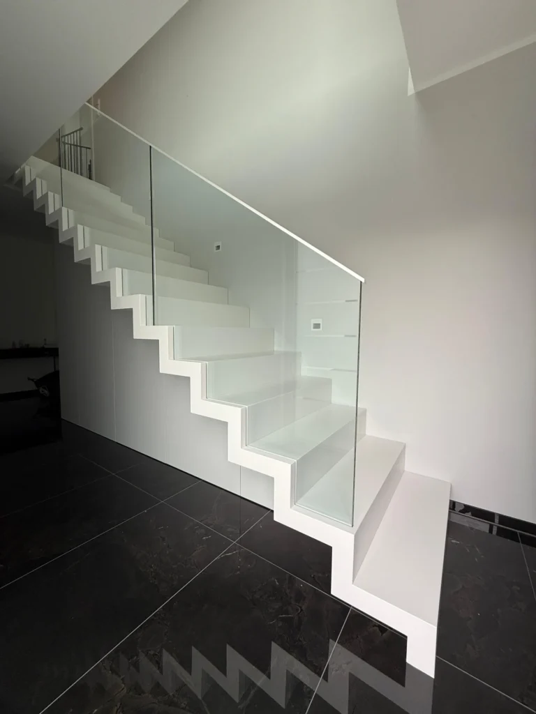 Minimalistische weiße Treppe mit geraden, kantigen Stufen und einem Glasgeländer vor einer weißen Wand und einem schwarzen, glänzenden Fliesenboden in einem modernen Innenraum.