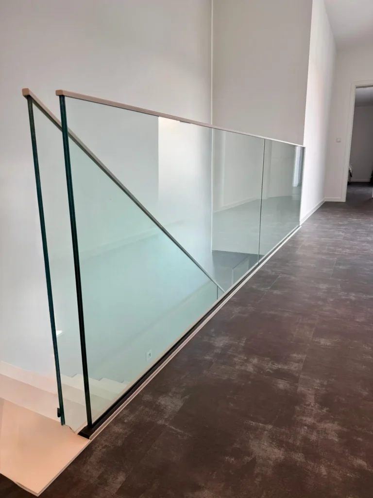 Ein moderner Flur mit dunklem Bodenbelag und einem Glasgeländer entlang einer Treppe, mit klaren, minimalistischen Linien und weißen Wänden.