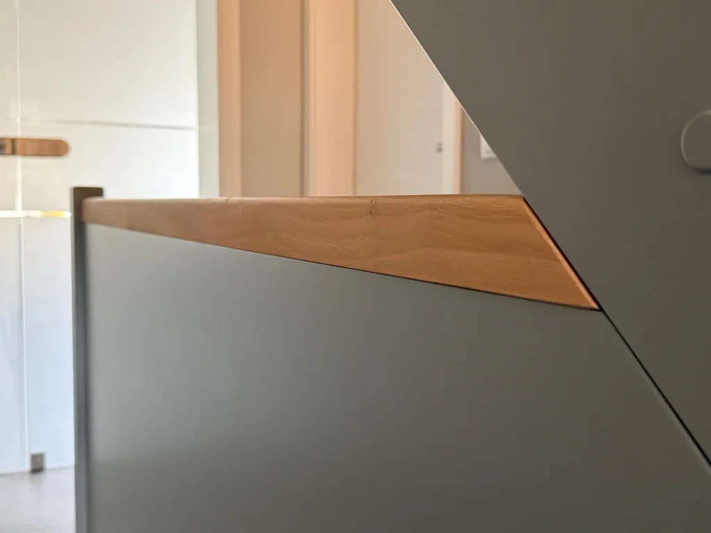 Eine Nahaufnahme einer modernen Treppe mit hellem Holzhandlauf und glatten grauen Seitenwänden, die in einem gut beleuchteten Innenraum klare Linien und minimalistische Designelemente hervorhebt.