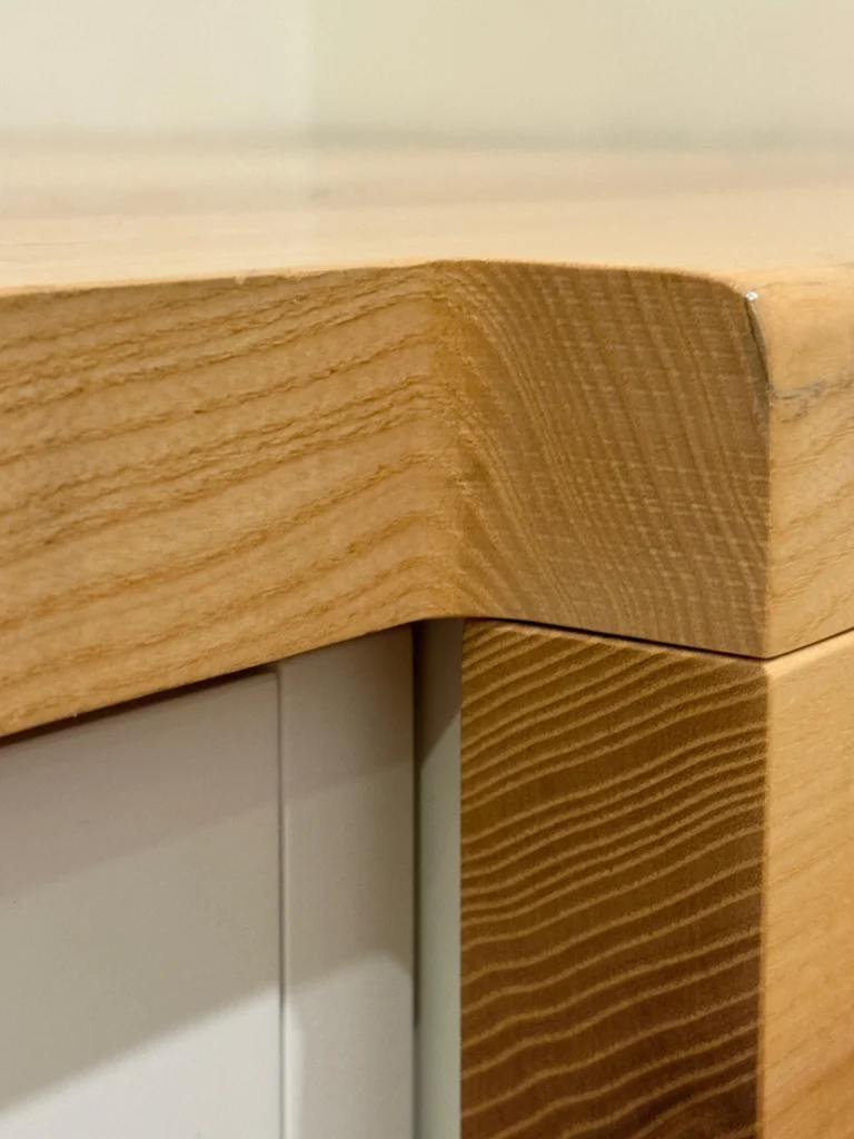 Nahaufnahme einer glatten, abgerundeten Arbeitsplatte aus Holz mit natürlicher Holzmaserung, die auf einem weißen Schrank angebracht ist.