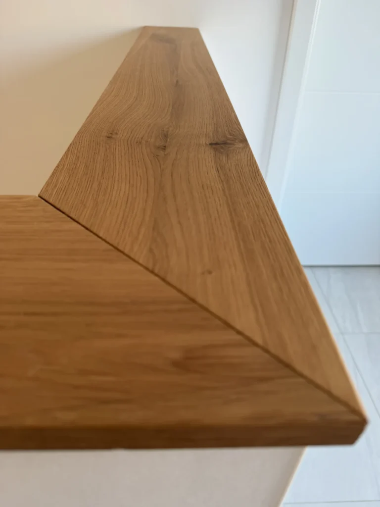 Nahaufnahme einer Holzoberfläche mit einer präzise gefügten Ecke, die die Holzmaserung und die saubere Winkelnaht zeigt, wahrscheinlich Teil eines modernen Innenmöbels oder eines Treppengeländers.