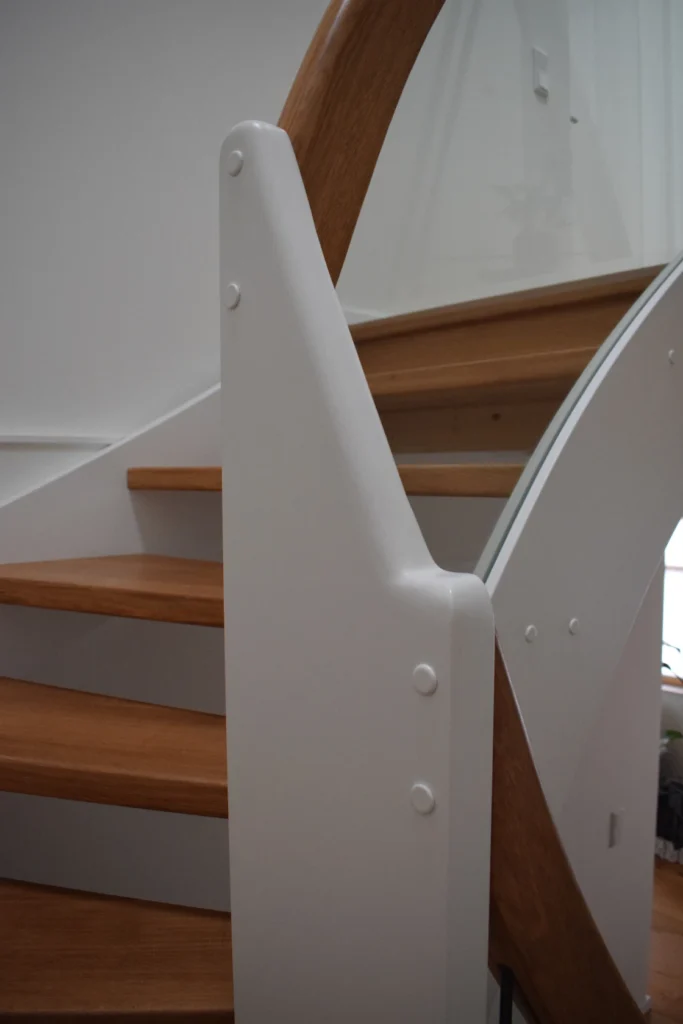 Nahaufnahme einer modernen Holztreppe mit weißen Wangen, abgerundeten Holzhandläufen und minimalistischem Design in einem gut beleuchteten Innenraum.