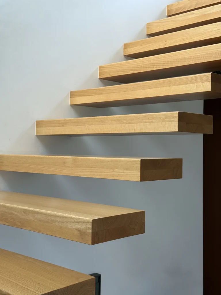Eine schwebende Holztreppe, die an einer weißen Wand befestigt ist, wobei jede Stufe wie ein massiver, rechteckiger Block ohne sichtbare Stützen wirkt und ein minimalistisches und modernes Design schafft.