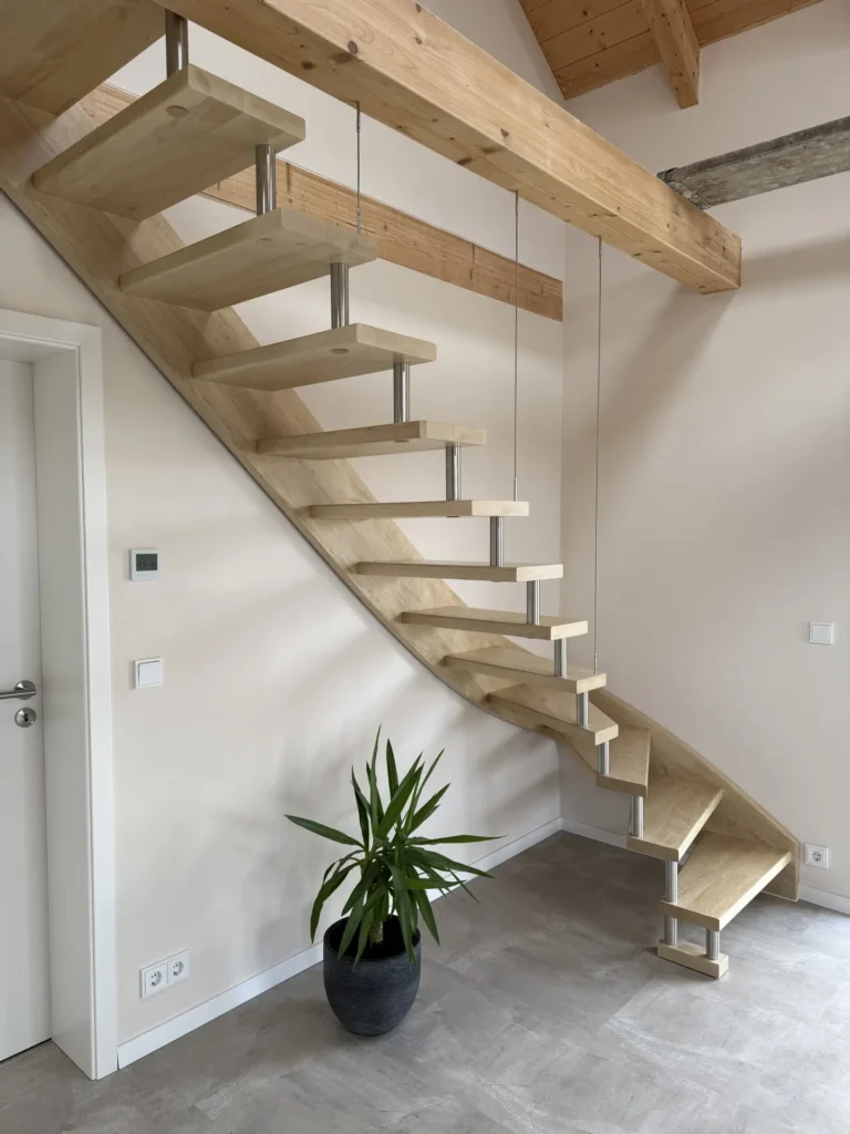 Moderne schwebende Holztreppe mit Metallstützen in einem minimalistischen Raum. Eine grüne Topfpflanze steht auf dem Boden unter der Treppe, neben einer weißen Tür an der linken Wand. Der Raum hat helle Wände und einen grauen Bodenbelag.