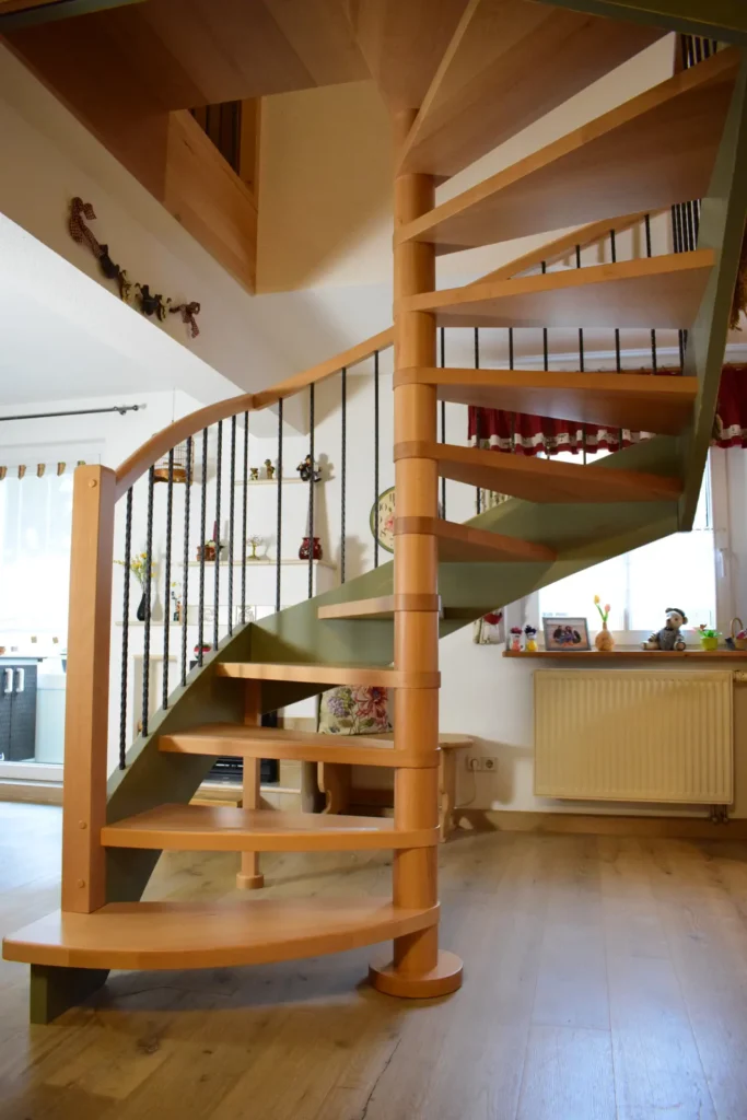 Eine spiralförmige Holztreppe mit grünen Akzenten in einem gemütlichen Wohnbereich mit Holzböden, einem Fenster mit roten Vorhängen und Regalen, die mit verschiedenen Ornamenten und Figuren dekoriert sind.
