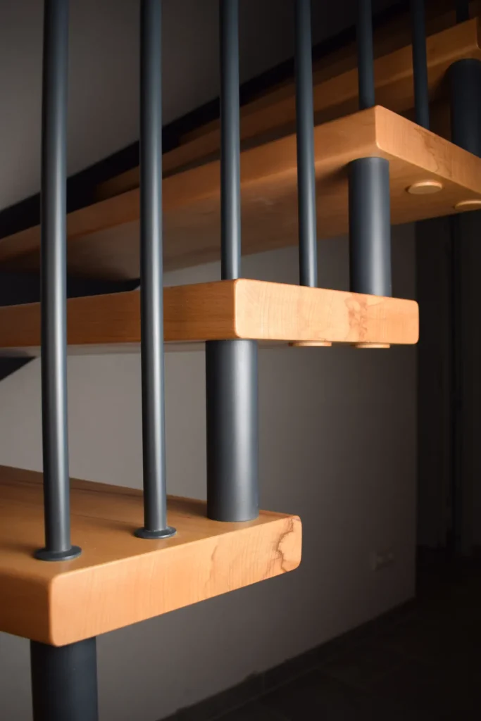 Nahaufnahme einer modernen Holztreppe mit vertikalem Metallgeländer, die die klaren Linien und das geometrische Design zeigt, vor einem neutralen Hintergrund.