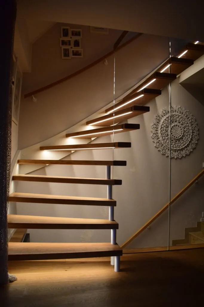 Eine moderne schwebende Holztreppe mit minimalem Geländer schlängelt sich nach oben und wird von eingebauten Leuchten unter jeder Stufe beleuchtet. An der Wand befinden sich gerahmte Fotos und ein dekoratives rundes Wandbild.