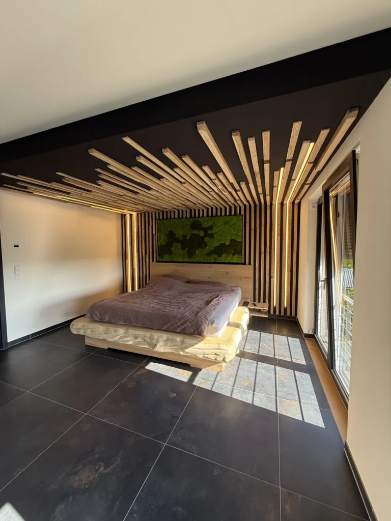 Ein modernes Schlafzimmer mit einem Podestbett, einer Wand- und Deckenverkleidung aus Holzlatten, großen Bodenfliesen, einem grünen Kunstwerk über dem Bett und Sonnenlicht, das durch die Glastüren auf der rechten Seite hereinströmt.