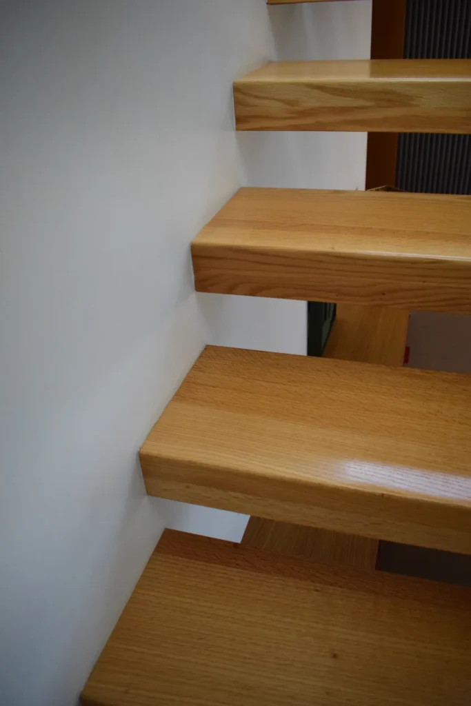 Nahaufnahme einer modernen, schwebenden Holztreppe, die an einer weißen Wand befestigt ist und ein minimalistisches und offenes Erscheinungsbild schafft.