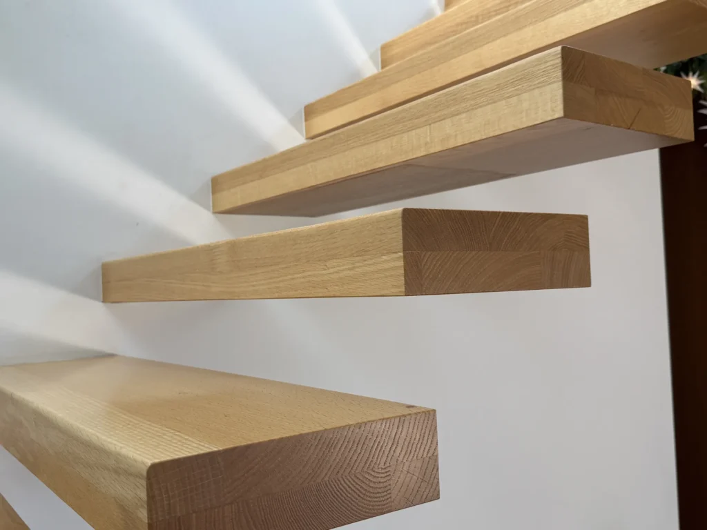 Nahaufnahme einer modernen, an einer weißen Wand befestigten schwebenden Holztreppe, die klare Linien und eine natürliche Holzmaserung zeigt.