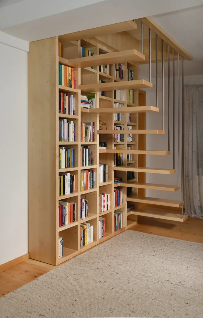 Eine moderne Holztreppe mit offenen Setzstufen ist in ein großes, mit Büchern gefülltes Regal integriert und verbindet so Stauraum und Treppe in einem minimalistisch gestalteten Raum mit hellen Holzböden und einem strukturierten Teppich.